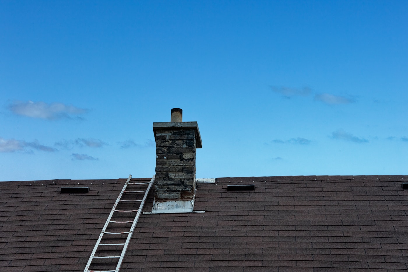 Chimney and ladder on a dark shingle roof