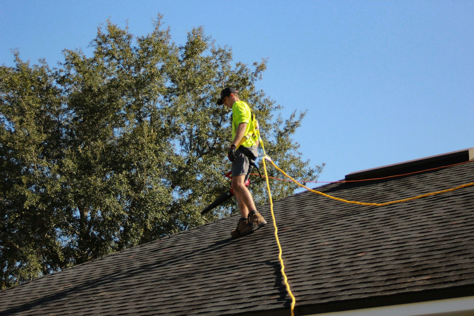 Roofer tied off with safety rope on a shingle roof